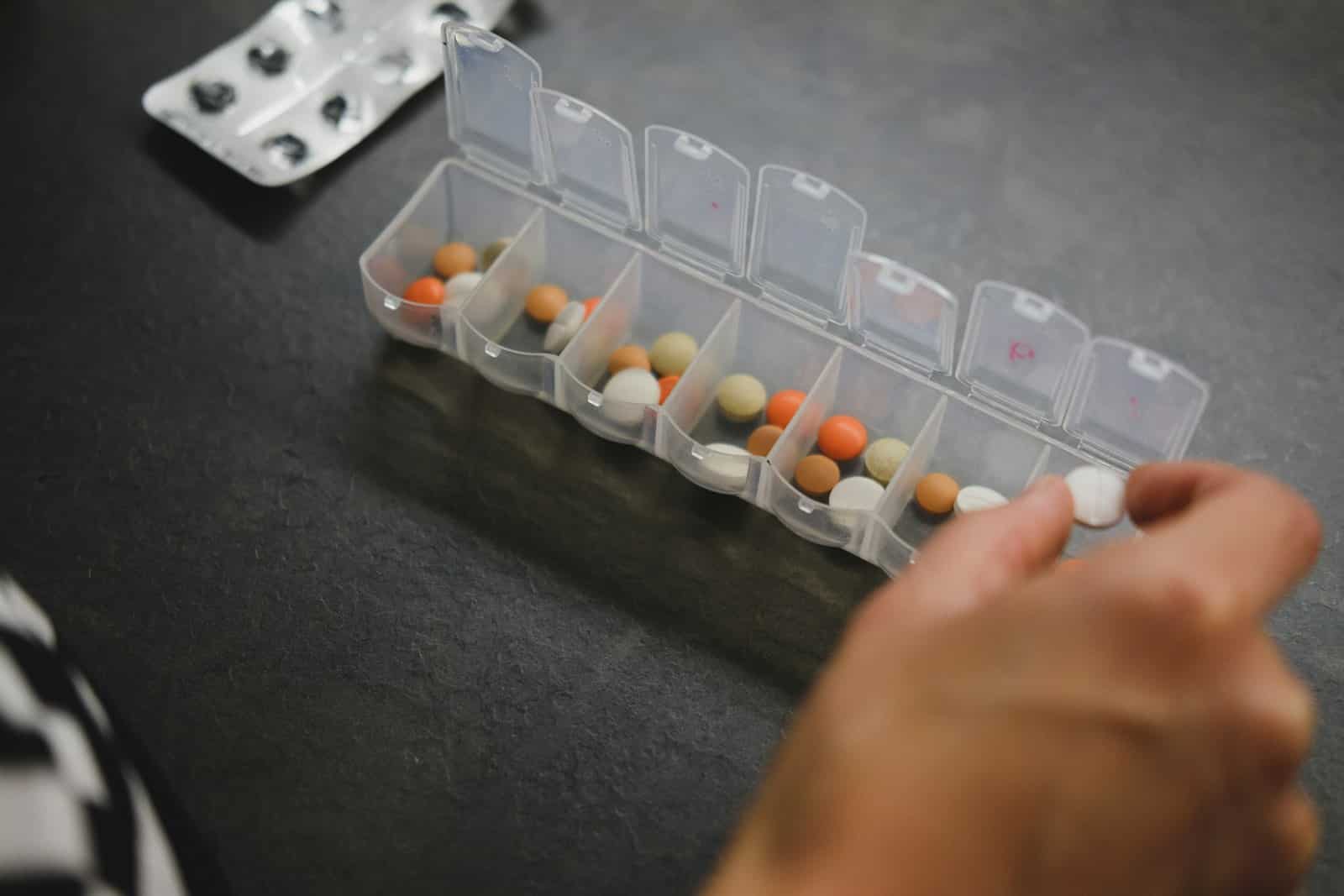 Mão pegando comprimidos em um porta-comprimidos com divisórias para os dias da semana